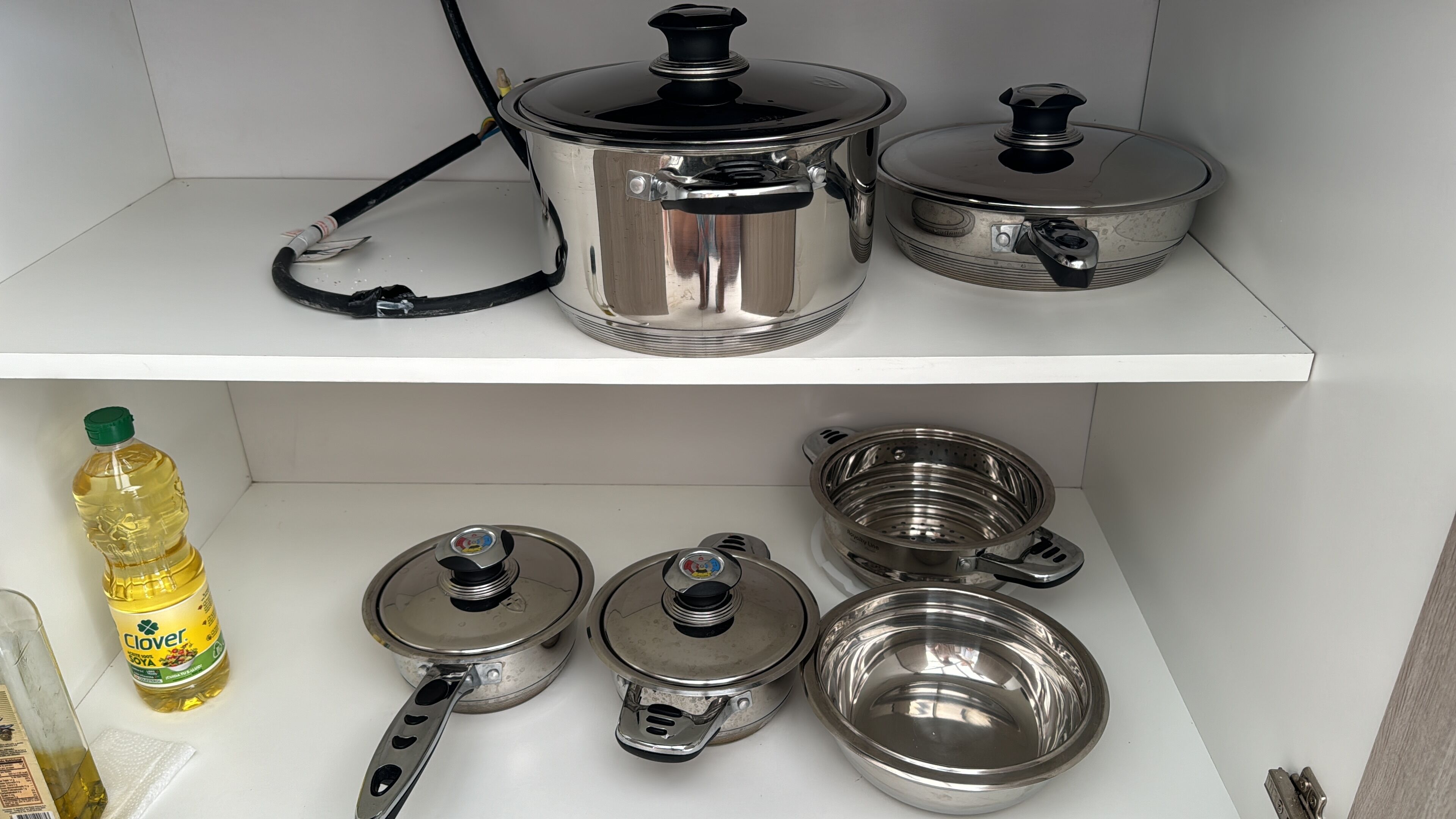 A kitchen with stainless steel cookware, including pots, pans, and a colander, neatly arranged on shelves.