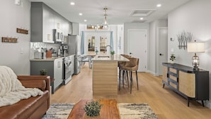 A modern kitchen with a central island, a dining area with a table and chairs, and a living room with a sofa and a coffee table.