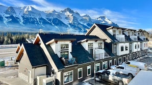 A row of modern buildings with a mountain backdrop, featuring a cross, parking area, and a clear sky.