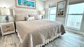 A bedroom with a large bed, two nightstands, a window with a view, and artwork on the walls. - Surfside #11, Beautiful Beachfront Luxury Condo,  Allergy Friendly:No Pets. (Mexico Beach)