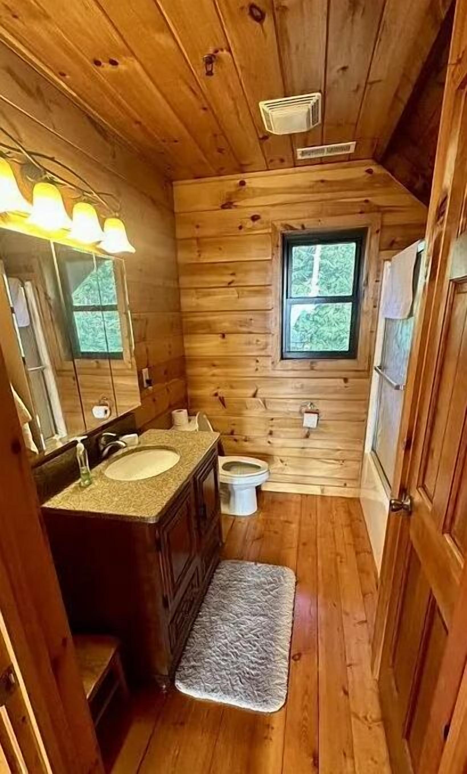 Een houten badkamer met een wastafelmeubel met dubbele wastafel, een toilet en een raam.