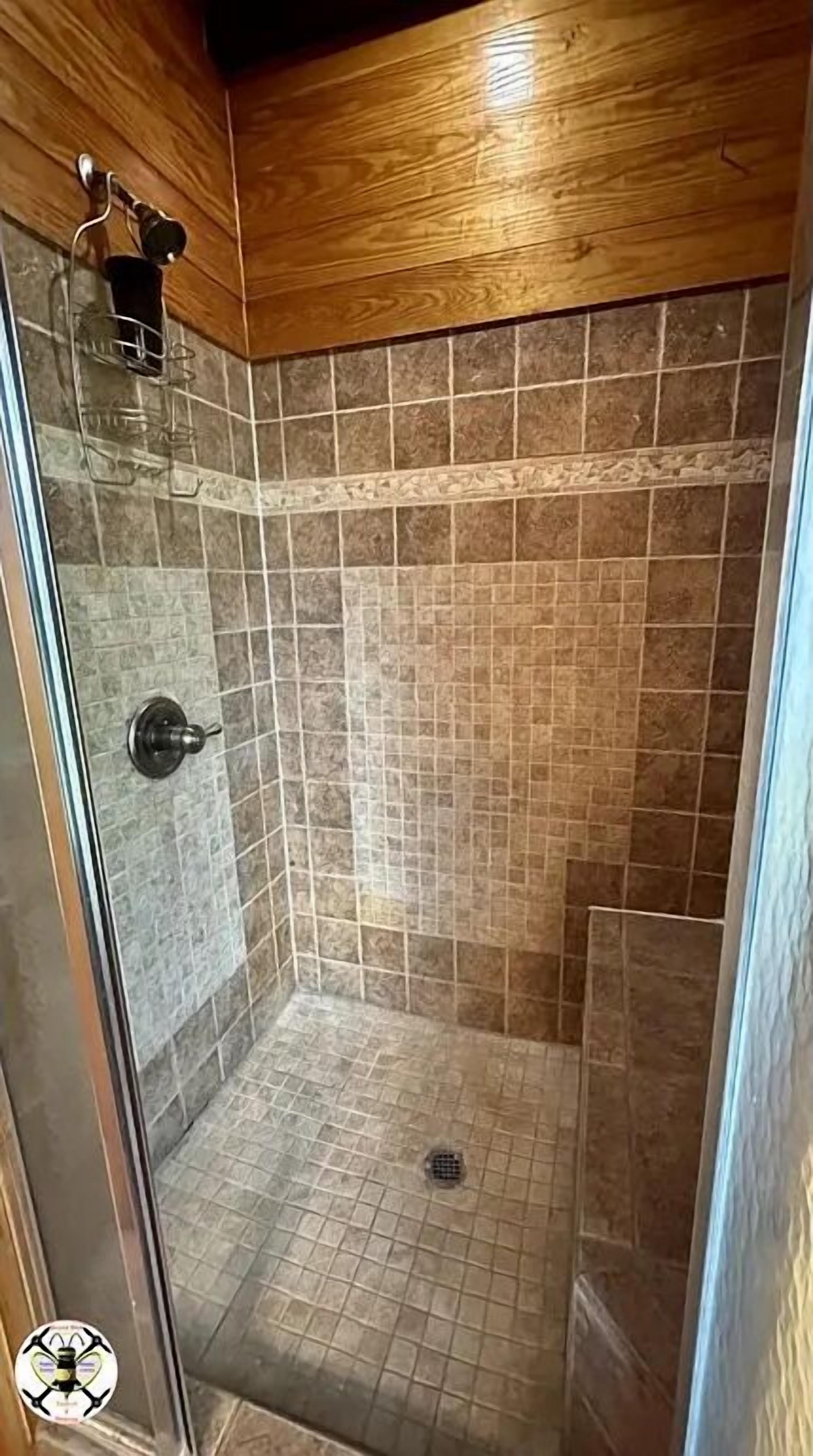 Une douche avec une porte en verre, des murs carrelés et un plafond en bois.