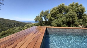 Eine Holzterrasse mit einem Pool, umgeben von Bäumen und Blick aufs Meer.