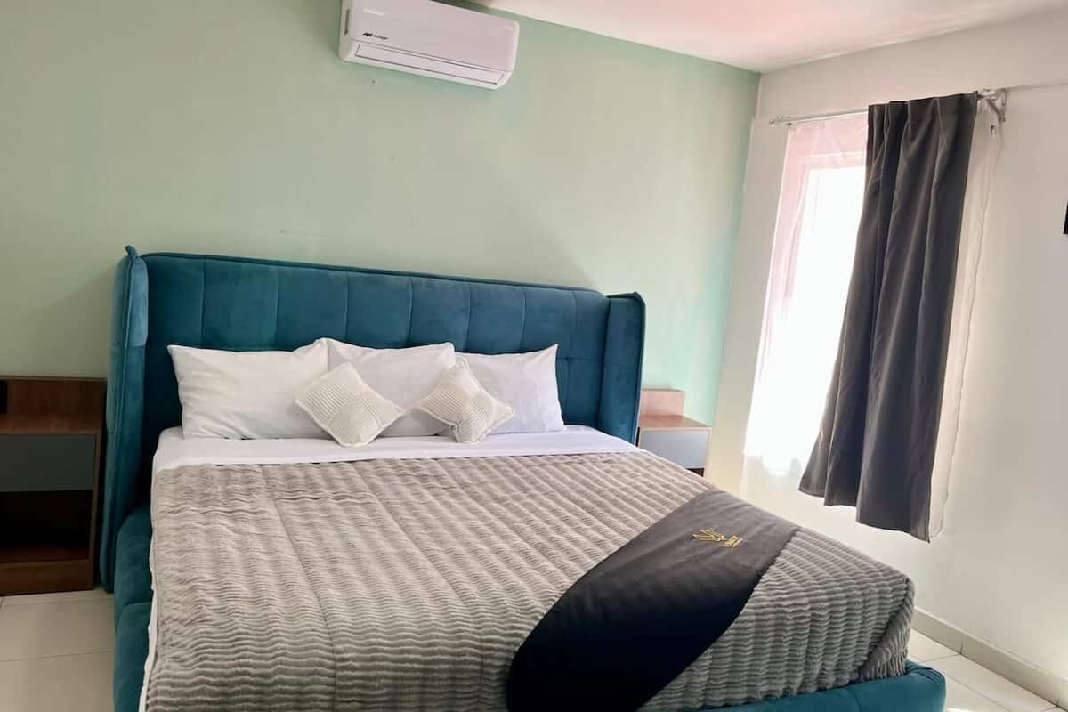 A bed with a teal headboard, white bedding, and a grey patterned blanket.