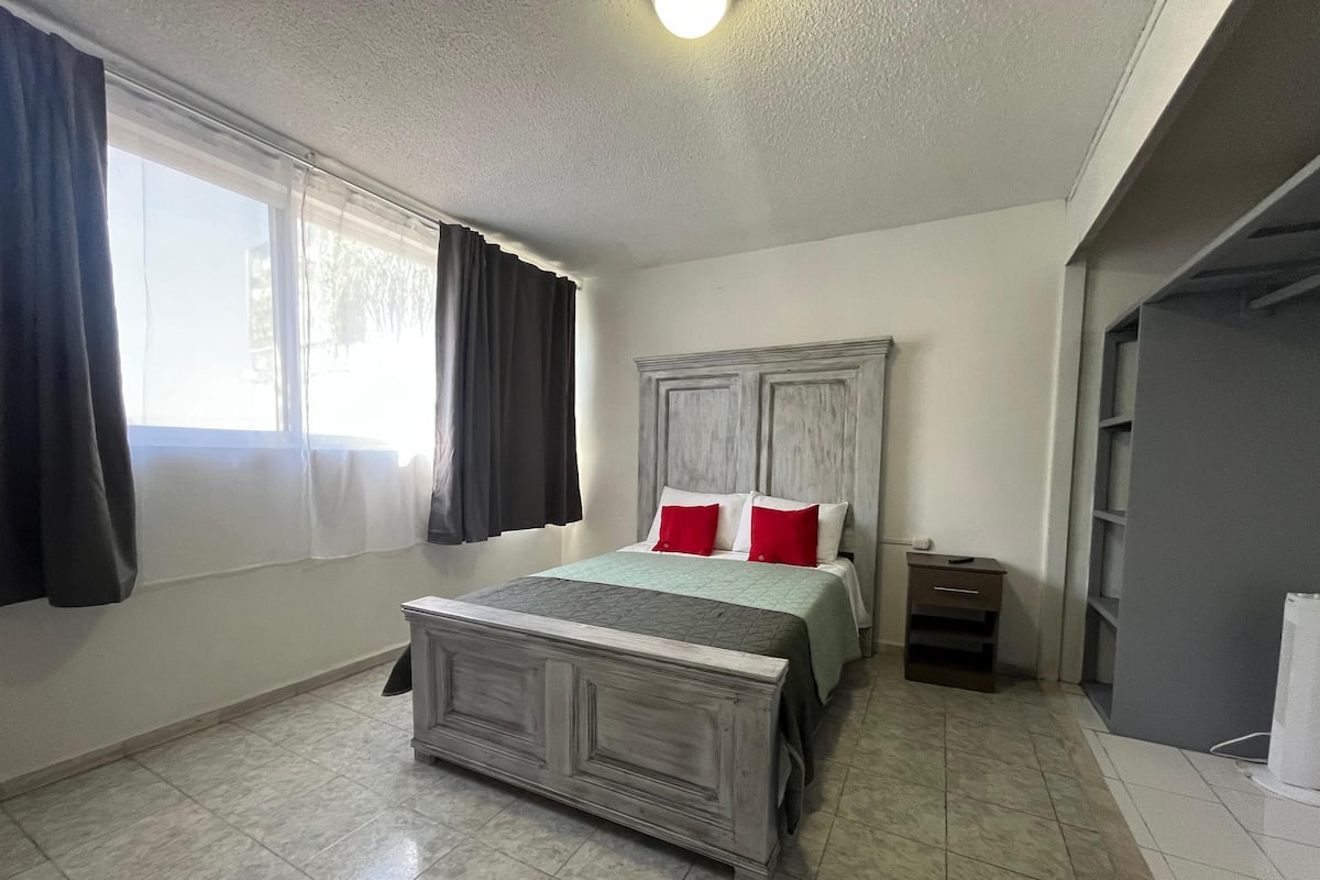 A bedroom with a bed, a nightstand, a wardrobe, and a window with curtains.