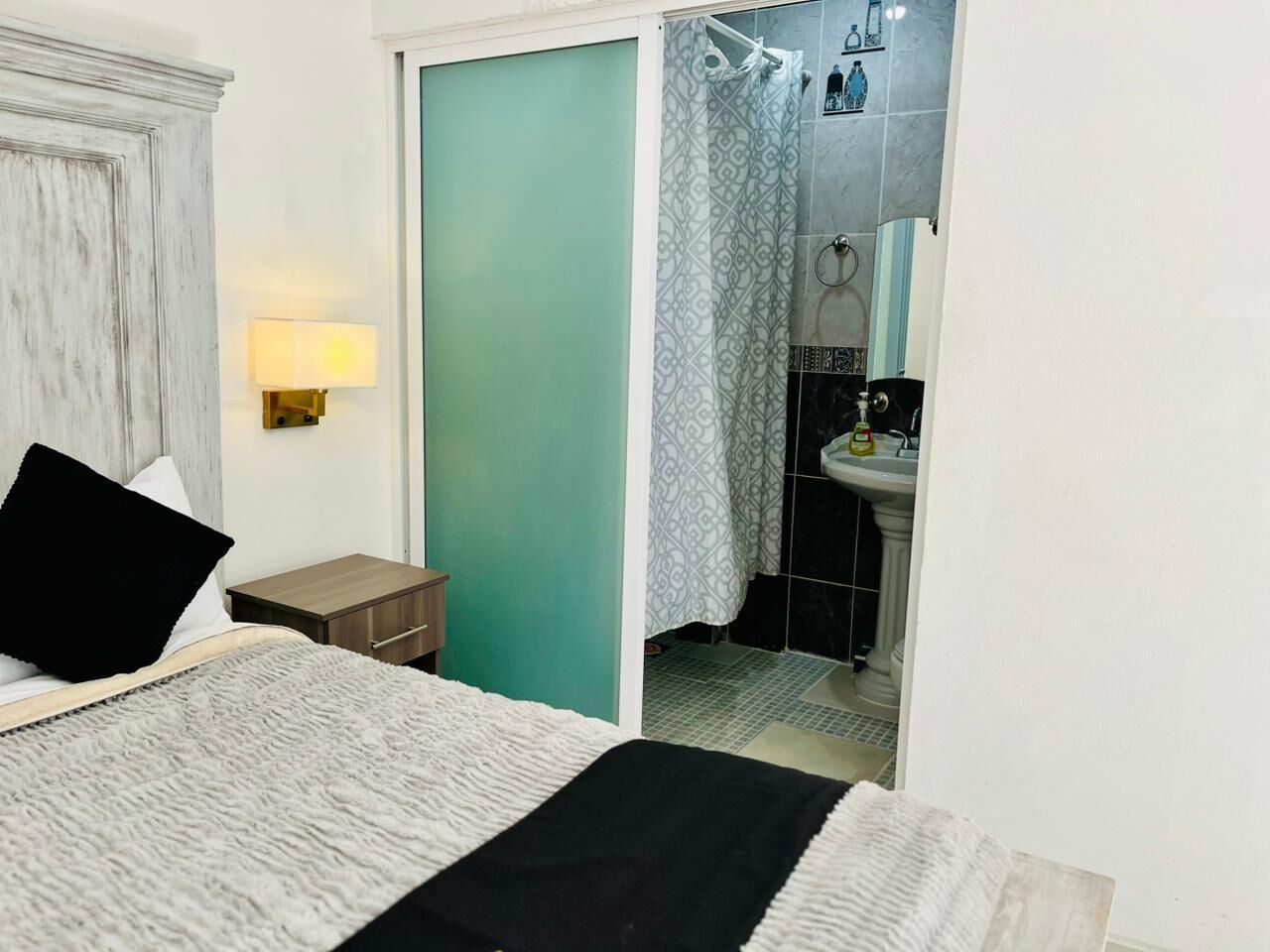 A bedroom with a bed, bedside table, and a view into the bathroom.