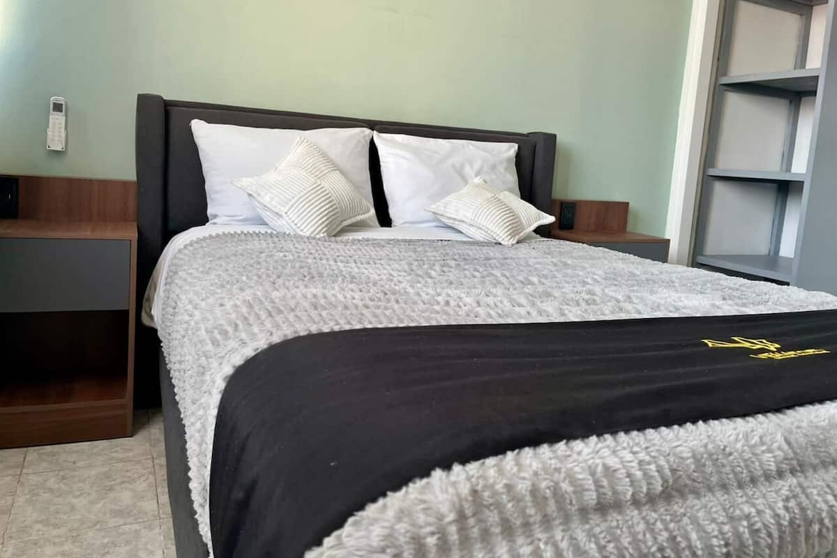 A neatly made bed with a white and black bedspread, two white pillows, and a wooden nightstand beside it.