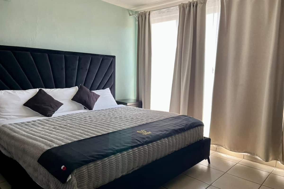 A neatly made bed with a dark headboard, white and dark pillows, and a quilted bedspread.