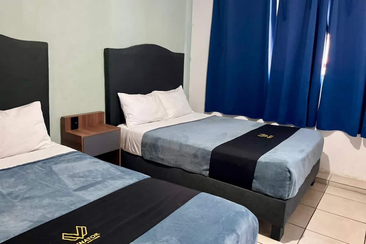 A hotel room with two beds, a nightstand, and a window with blue curtains.