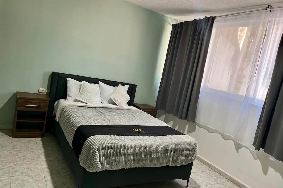A neatly arranged bedroom with a bed, bedside tables, and a window with curtains.