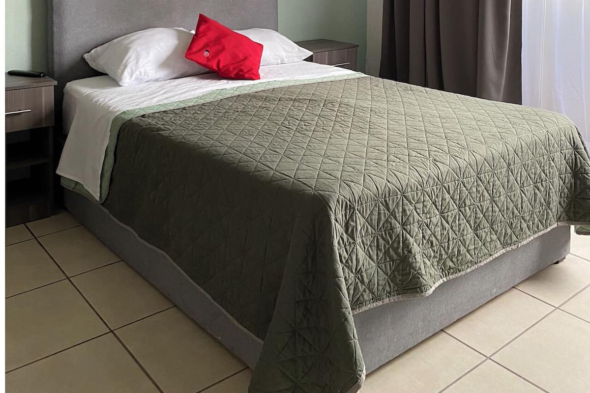 A bed with a grey headboard, white and red pillows, and a green quilted bedspread.