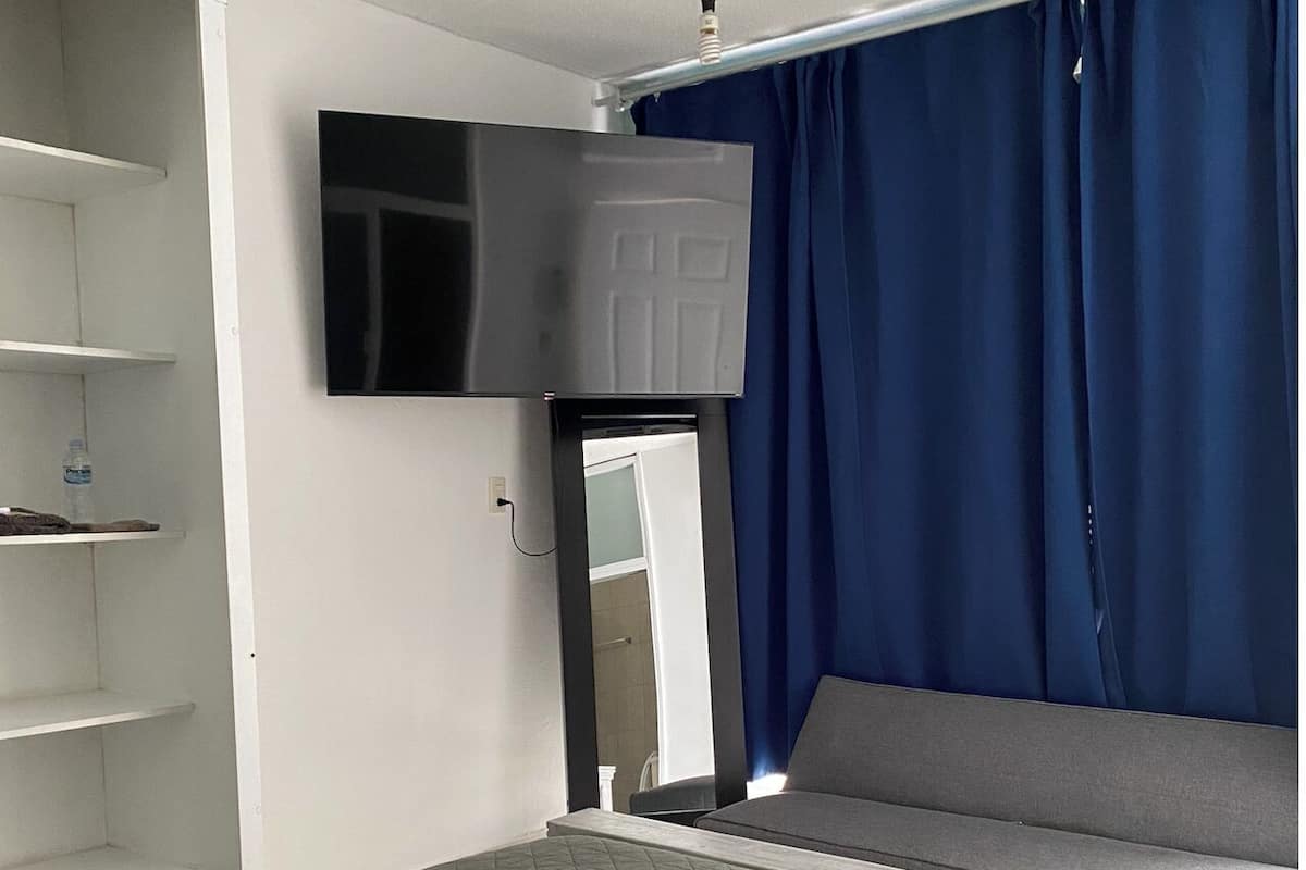 A hotel room with a bed, a TV mounted on the wall, a wardrobe, and a window with curtains.