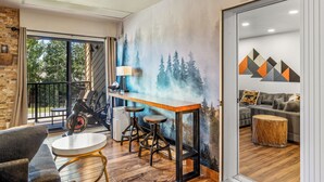 A modern living room with a large window, a staircase, a bar area with stools, and a couch. - Large Luxury: Fun 4 the Whole Family. 2 min walk to Slopes. Hot Tubs. Pool Table (Steamboat Springs)