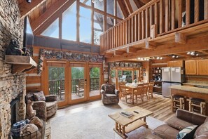 A spacious living area with a stone fireplace, wooden furniture, a dining table, and a kitchen area.