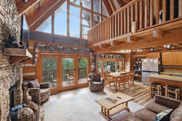 A spacious living area with a stone fireplace, wooden furniture, a dining table, and a kitchen area.