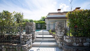 Ein Steintor führt zu einem Haus mit einem Ziegeldach, einem Schwimmbecken und einer Steinsäule an der Seite.
