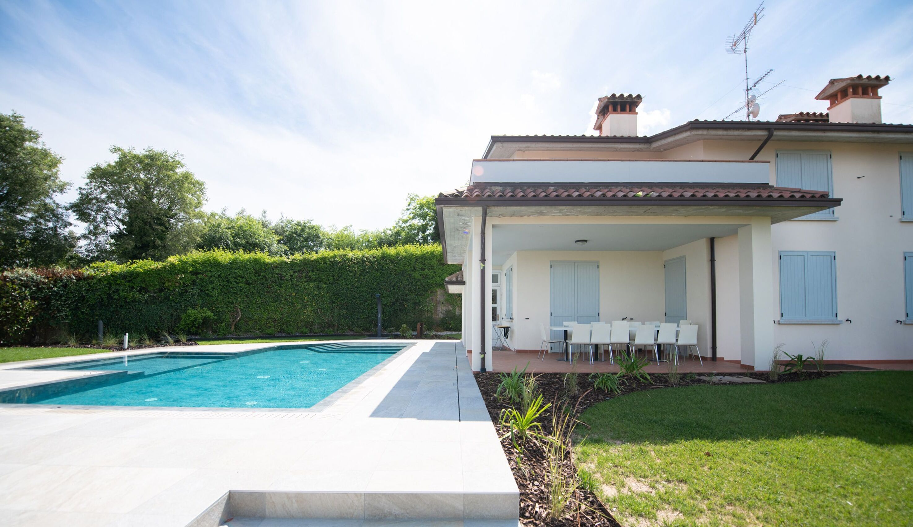 Una casa de dos pisos con piscina, un patio cubierto con mobiliario exterior y un jardín bien cuidado.