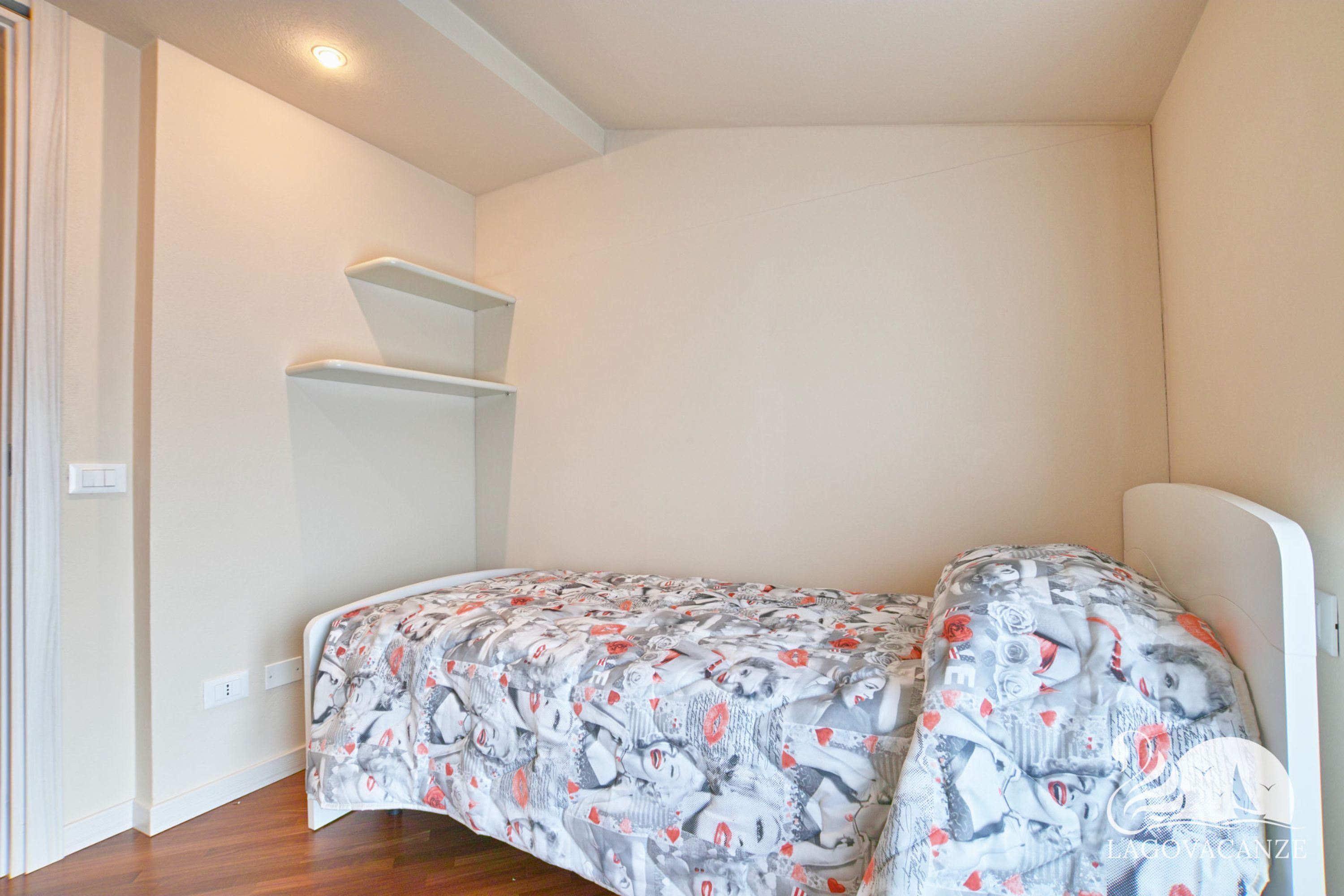 Une petite chambre à coucher, bien rangée, avec un lit, une étagère et une porte.