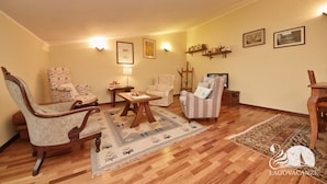 Ein Wohnzimmer mit Holzboden, einem gemusterten Teppich und verschiedenen Sitzmöglichkeiten, darunter ein Schaukelstuhl, Sessel und ein Streifenstuhl.