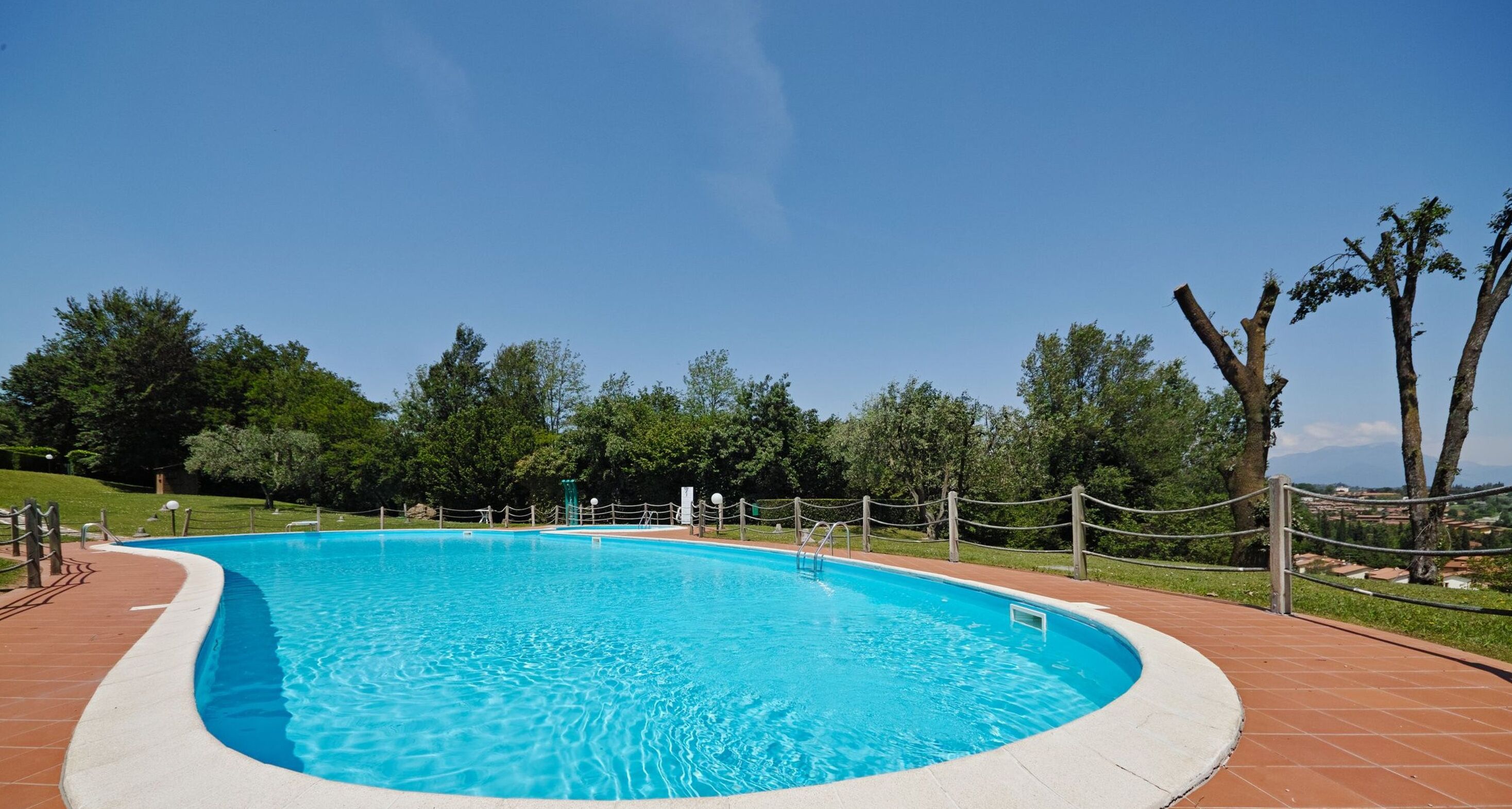 Une piscine rectangulaire bordée de carreaux, entourée d’une clôture en bois et d’un chemin piétonnier en briques.