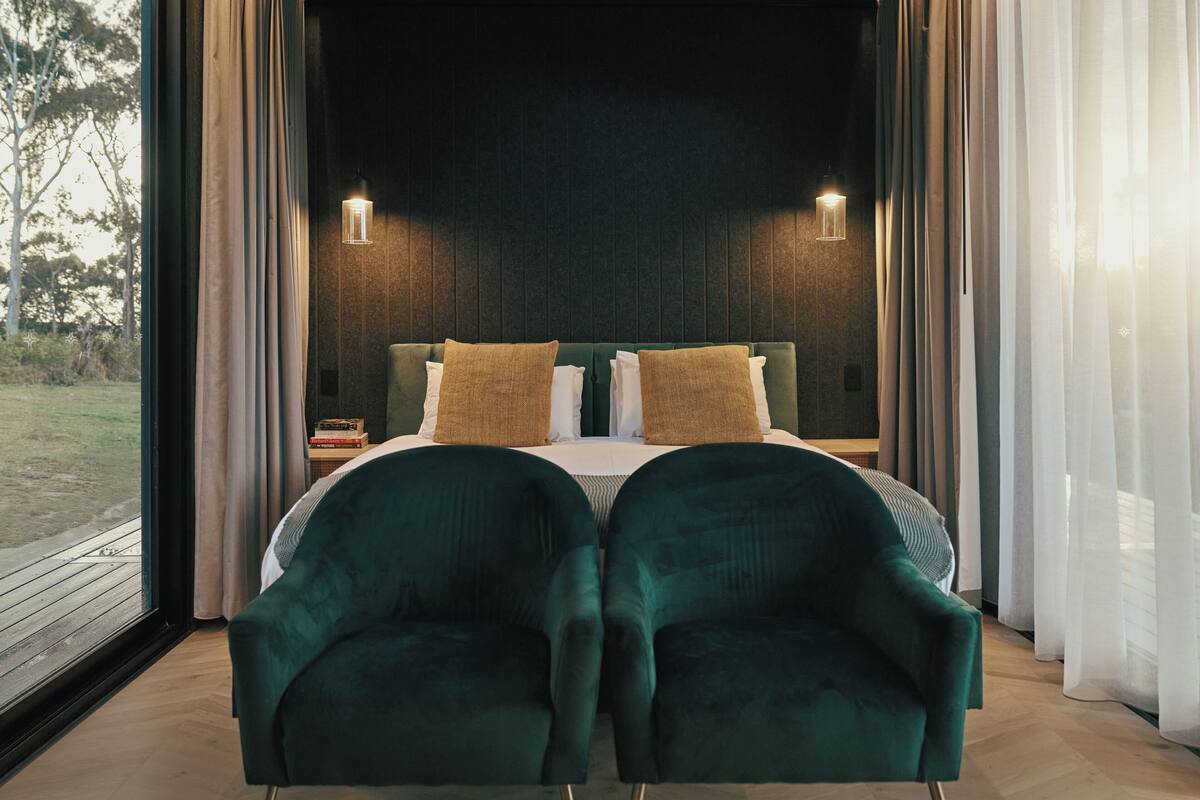 A bedroom with a bed, two chairs, a nightstand, and two wall-mounted lights.