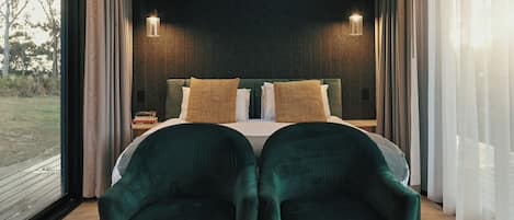 A bedroom with a bed, two chairs, a nightstand, and two wall-mounted lights.