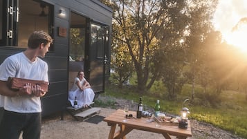 Un espacio de comedor al aire libre con encanto, con una mesa de madera dispuesta para una comida, una botella de vino y un farol.