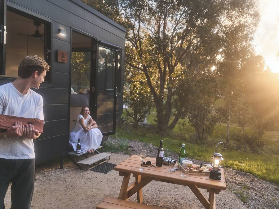 A rustic outdoor dining area with a wooden table set for a meal, a bottle of wine, and a lantern.