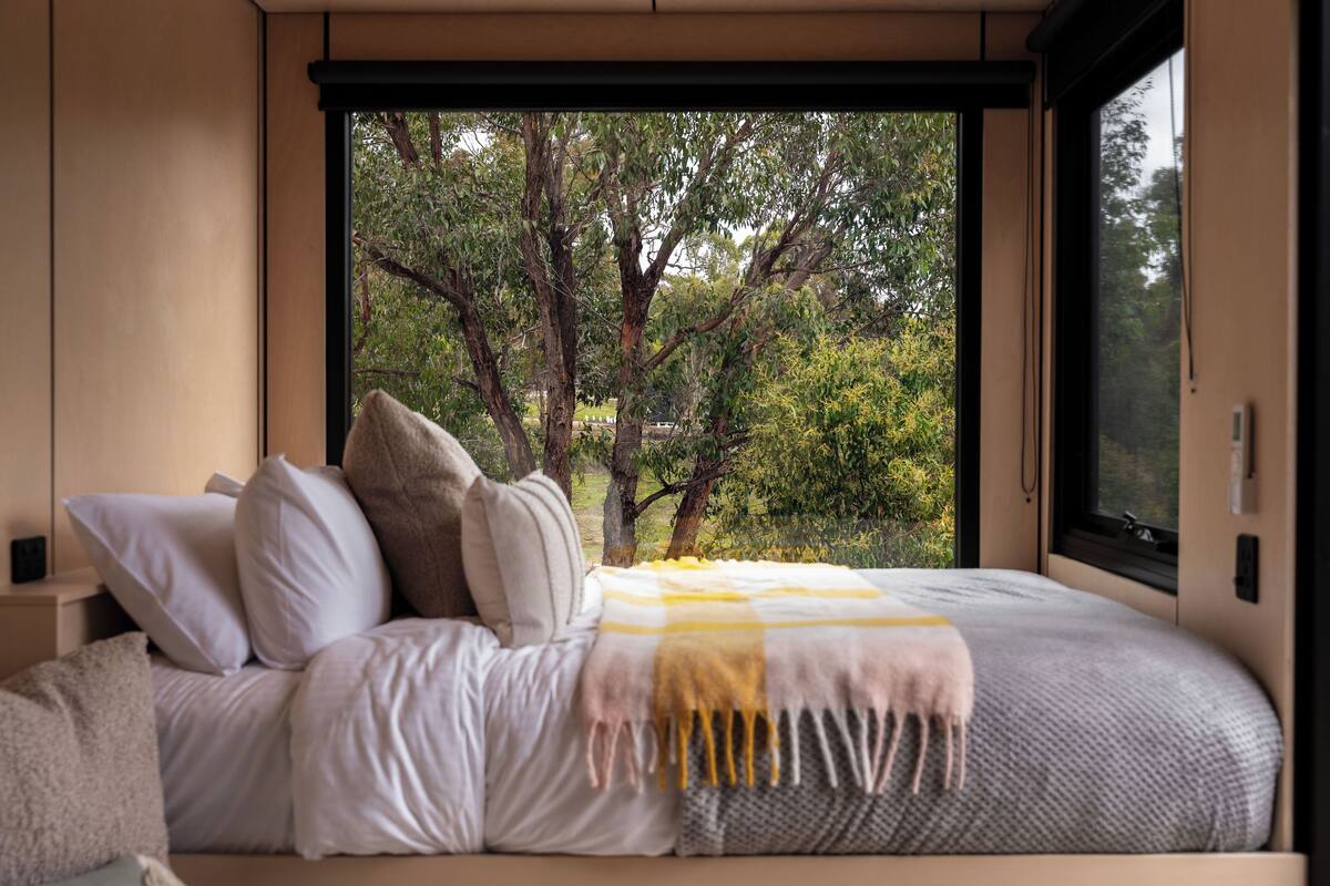 A bedroom with a large window, a bed with white bedding, and a view of trees outside.
