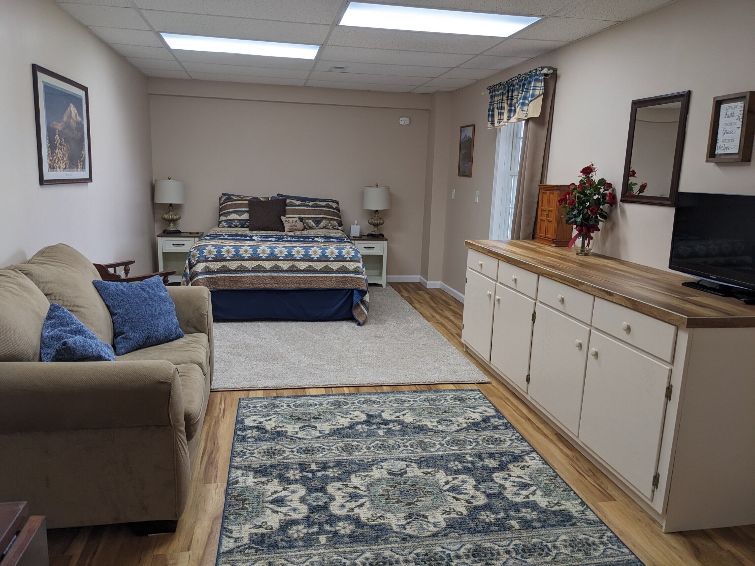 A bedroom with a bed, a dresser, a television, and a sofa.