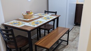 Un comedor con una mesa de madera, cuatro sillas y un banco. Se ve un refrigerador al fondo.