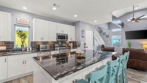 A modern kitchen with white cabinets, a black marble island, and teal chairs. - Canal Front | Gated Community, Firepit & Decks (Port Bolivar)