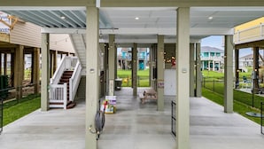 A covered outdoor area with concrete flooring, wooden picnic tables, and a white railing. - Canal Front | Gated Community, Firepit & Decks (Port Bolivar)