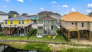 A waterfront residential area with colorful houses, some with balconies, and a small dock extending into the water. - Canal Front | Gated Community, Firepit & Decks (Port Bolivar)
