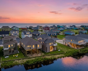 A coastal residential area with houses, some elevated on stilts, and a body of water in the foreground.