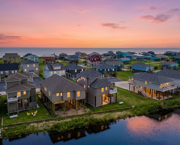A coastal residential area with houses, some elevated on stilts, and a body of water in the foreground.