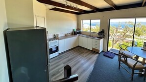 A modern kitchen with a gas stove, microwave, and sink, wooden beams on the ceiling, and a view of the outdoors through large windows. - Little Innes - affordable accommodation with a view (PORT ALBANY)