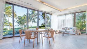 Une pièce spacieuse avec une grande table à manger et des chaises, un canapé et une vue sur les palmiers et l’océan.