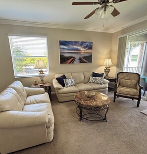 A living room with a sofa, a coffee table, a chair, and a ceiling fan. - Heritage Pointe Condo, Fort Myers (Fort Myers)