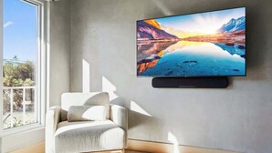Un salon moderne doté d’un grand téléviseur à écran plat fixé au mur, d’un fauteuil confortable et d’une grande fenêtre offrant une vue sur l’extérieur.