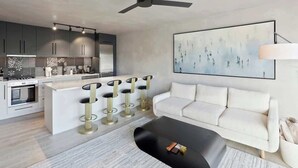 Un salon moderne avec un canapé blanc, une table basse noire et une cuisine en arrière-plan.