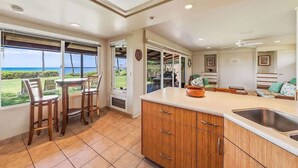 A kitchen with a large island, a dining area with chairs, and a view of the ocean. - Beach front Honu Cottage (Kihei)