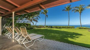 A covered outdoor area with lounge chairs, a well-maintained lawn, and a view of the ocean. - Beach front Honu Cottage (Kihei)