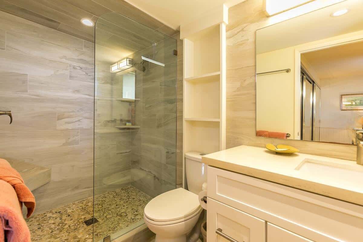 A modern bathroom with a glass-enclosed shower, a toilet, and a vanity with a mirror.