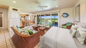A spacious living area with a large bed, wicker furniture, and a view of the outdoors. - Beach front Honu Cottage (Kihei)
