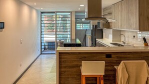 A modern kitchen with a large island, wooden cabinets, and a view through a glass door. - Edificio Atalanta (Medellín)
