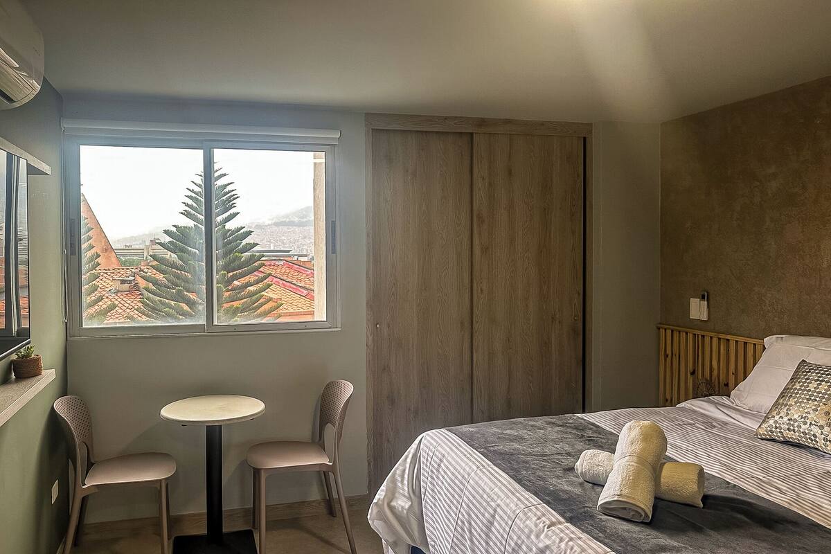 Ein Schlafzimmer mit einem Bett, einem Fenster mit Blick auf Gebäude, einem kleinen Tisch und zwei Stühlen.