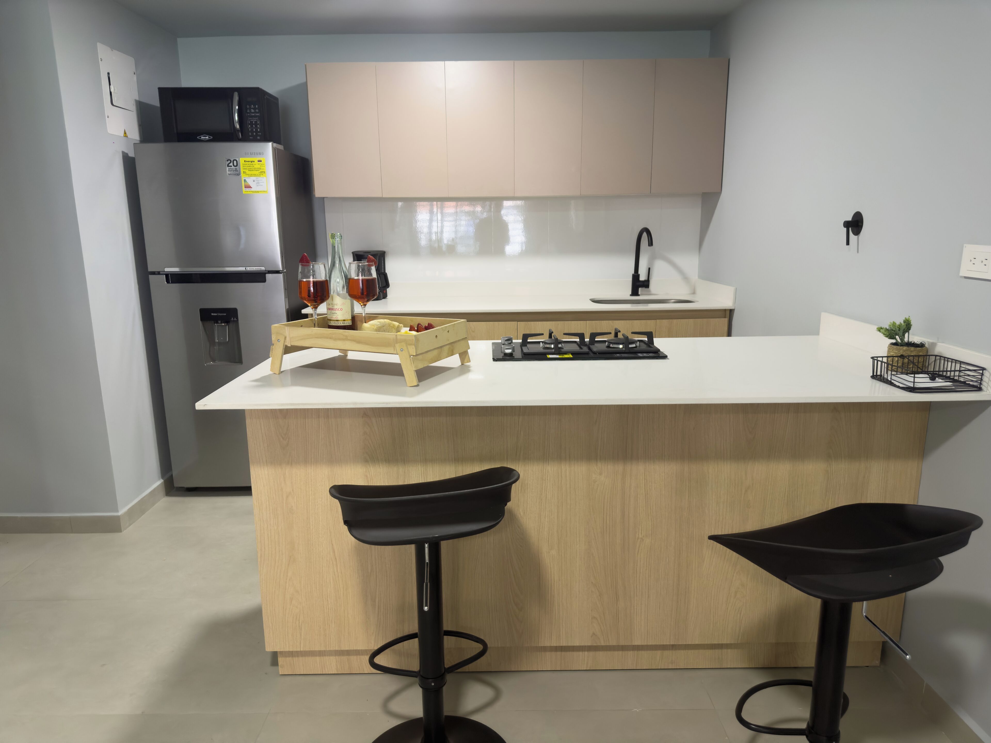 Una cucina moderna con un'isola centrale, due sgabelli da bar, un frigorifero, un lavello e un fornello.