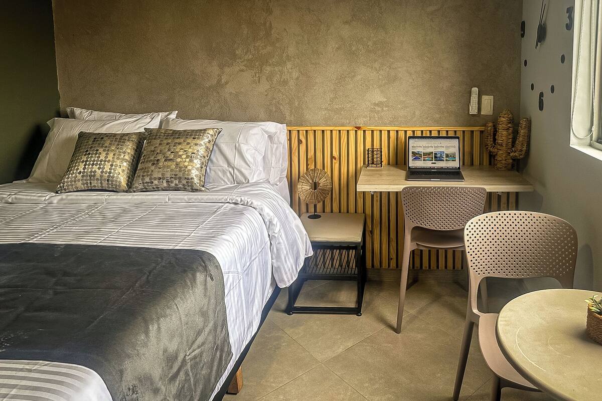 Ein Schlafzimmer mit einem Bett, einem Schreibtisch mit Laptop, einem Sessel und einem kleinen Tisch.