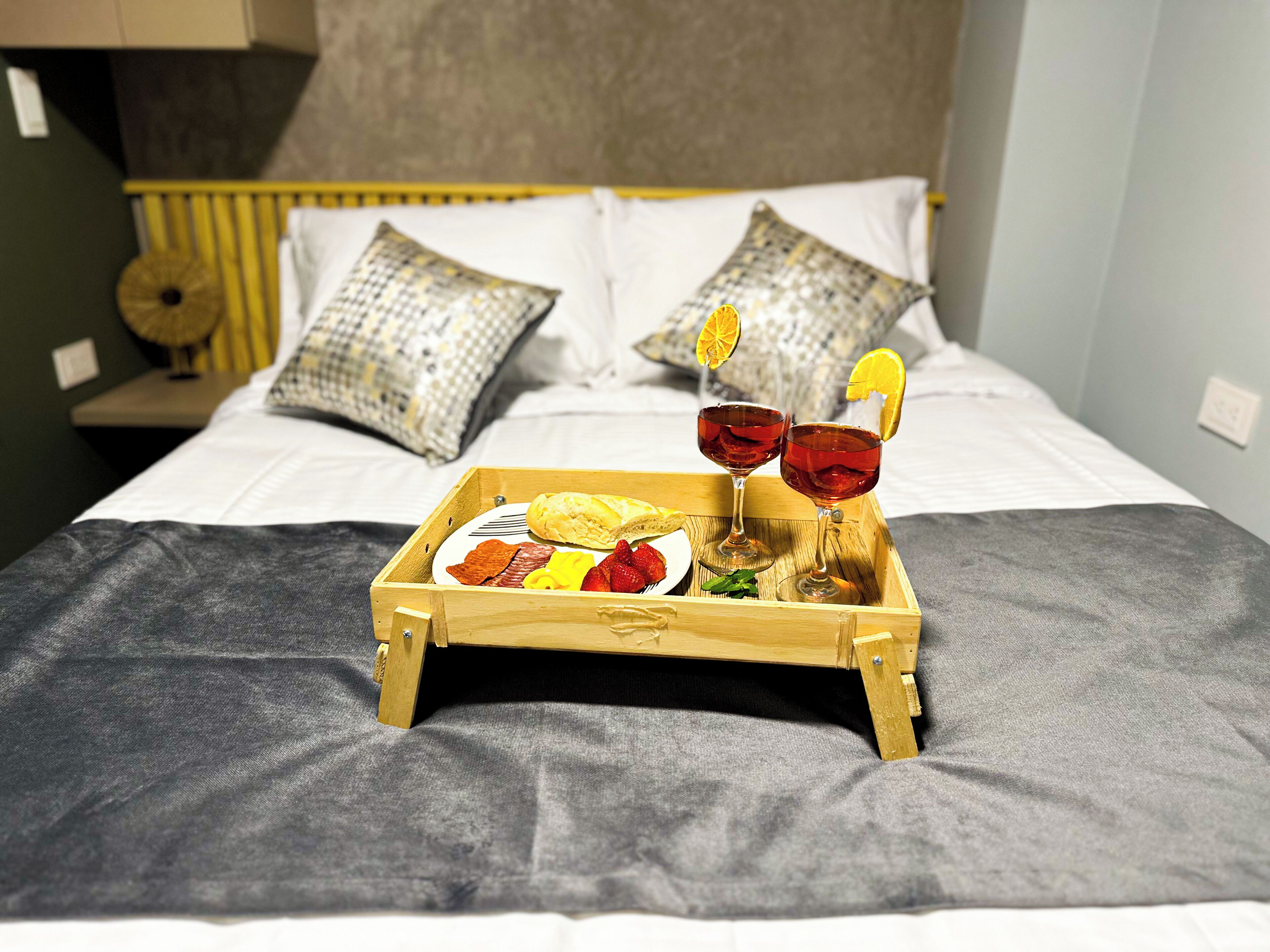 A wooden tray with food and drinks on a bed.